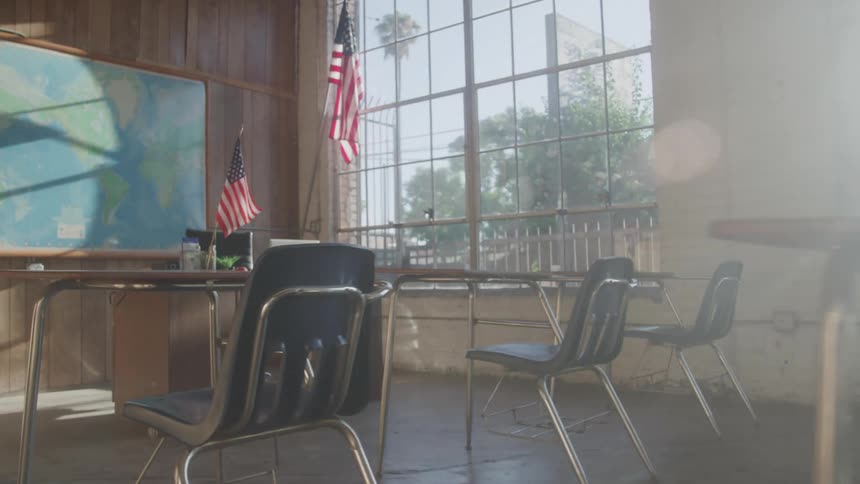 An empty sunlit classroom with old desks and american flags