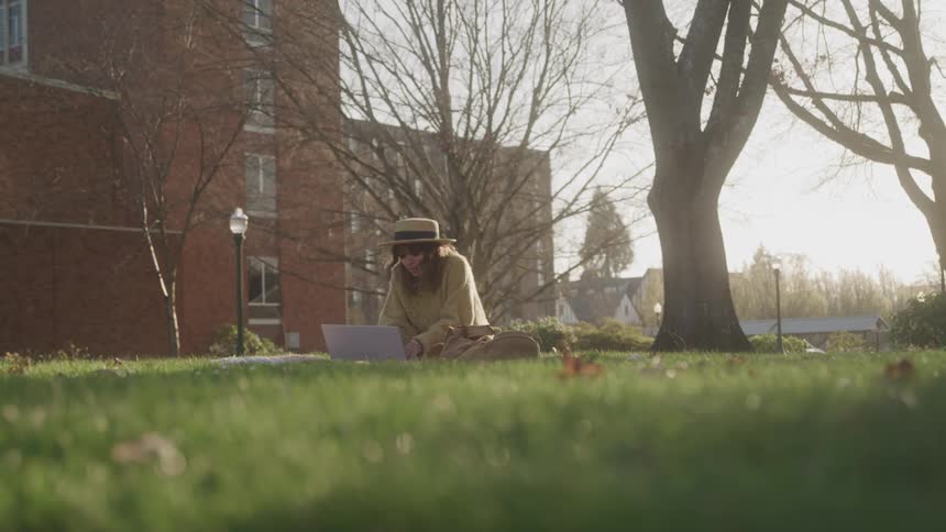 Woman works on a laptop while sitting on the lawn on an autumn day