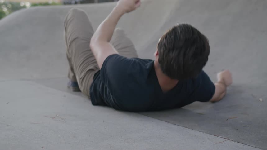 A young adult male stands up from a concrete floor skating rink outdoors during daytime