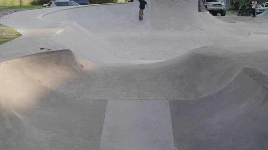 A skateboarder glides smoothly over the curved ramps of an empty concrete skatepark