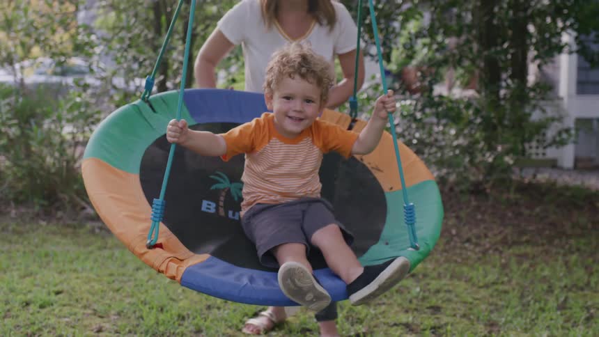 Mother and son both smile while she pushes him on a swing