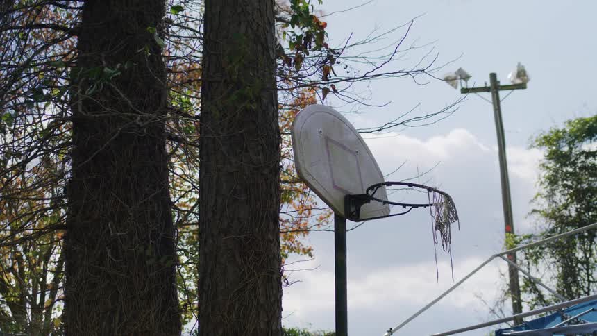 Worn basketball hoop with torn net in a treelined outdoor area