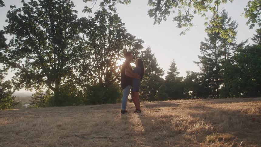 Couple slow dance in a field with sunlight shining through tree branches