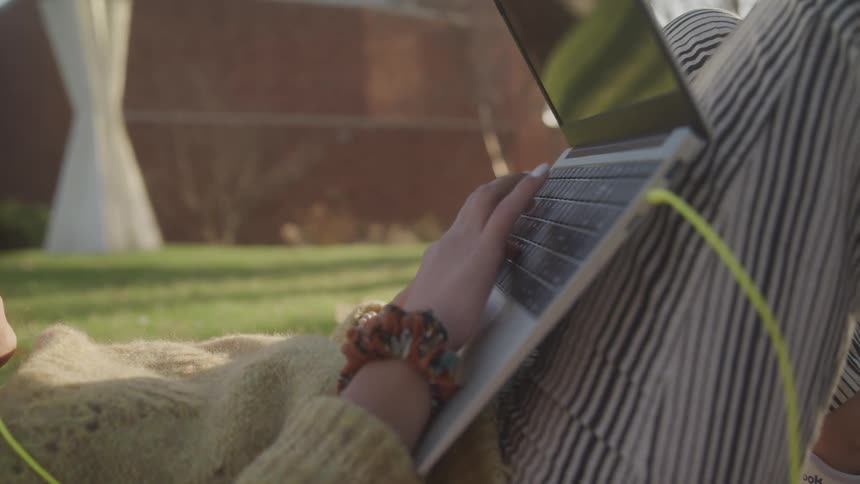 A woman lies on a lawn using her laptop at midday
