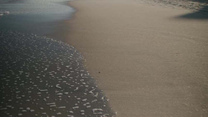 Sea foam gently washes over the sandy beach