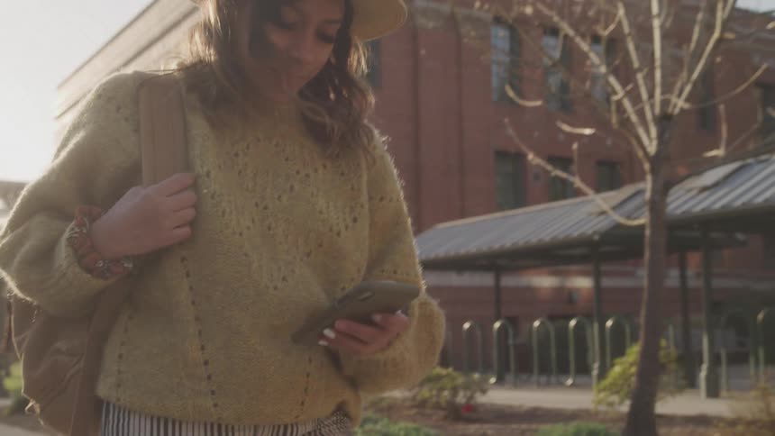 Woman walking outdoors and typing on a smartphone