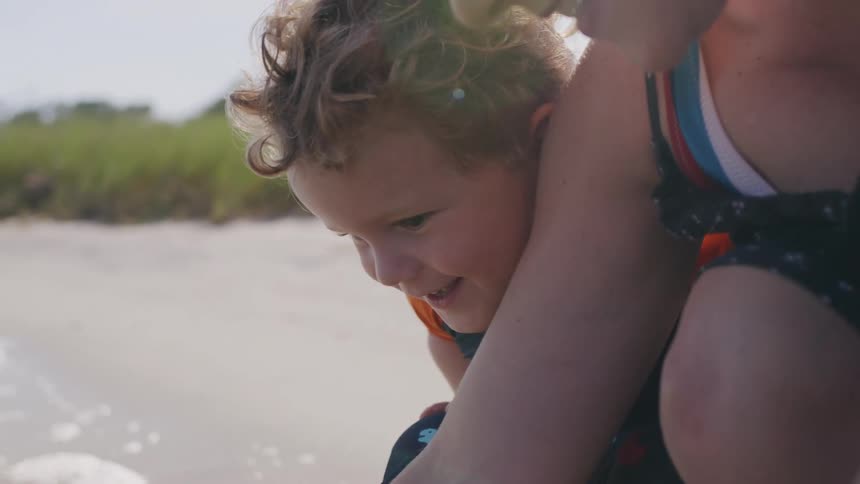 A joyful mother and her young son play together on a sunny beach
