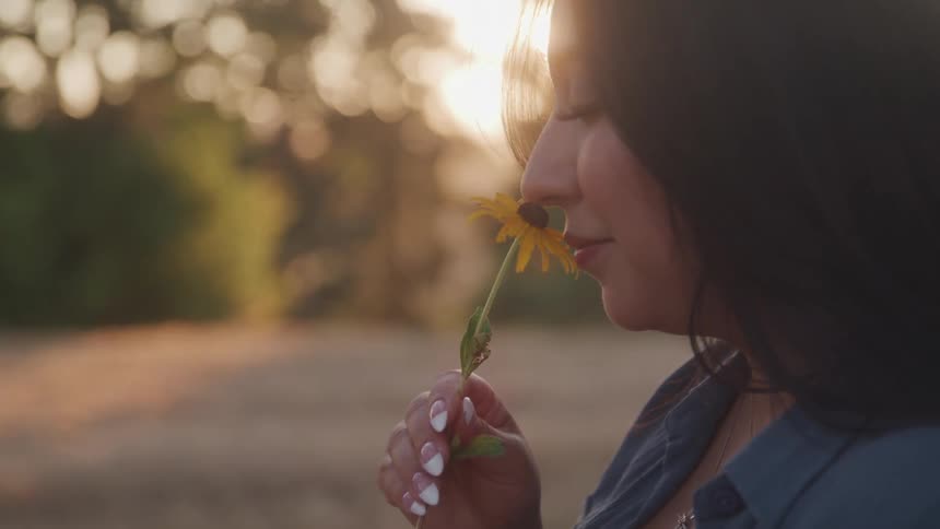 Longhaired woman smells a yellow flower at sunset