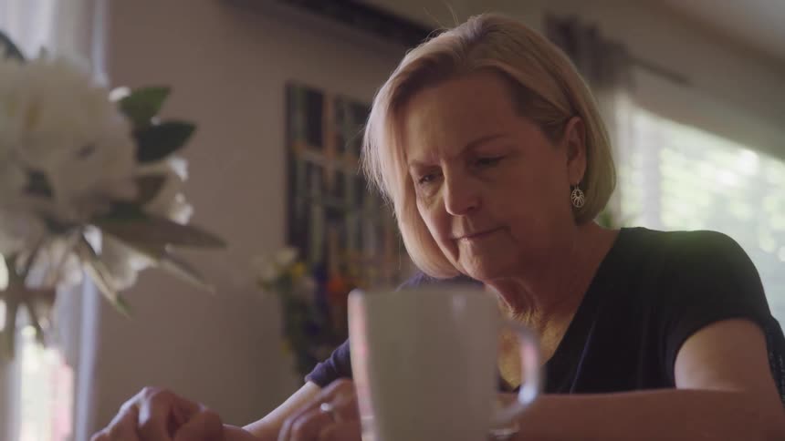 Woman with short blonde hair writes at a table with a mug in front