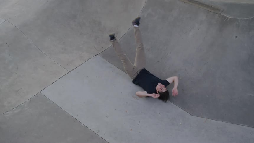 A man on a skateboard rides down a concrete ramp then falls and lies on his back