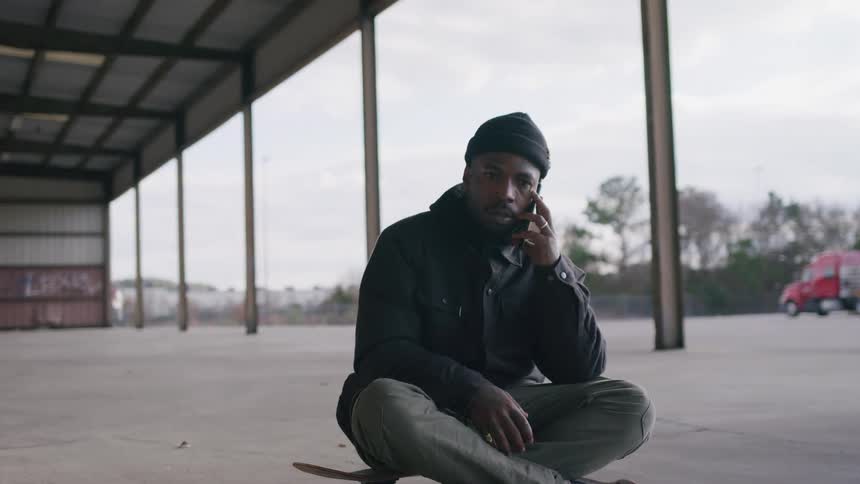Man sitting on a skateboard talks cheerfully on the phone