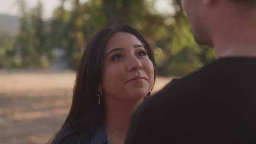 A woman with long dark hair and a nose ring gazes up smilingly at a man during an outdoor moment