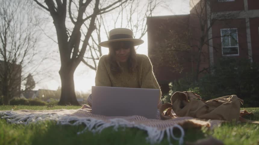Woman lies on blanket in park using laptop