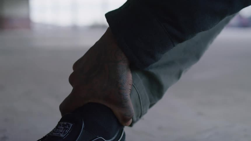 Tattooed hand adjusts the lace of a black sneaker