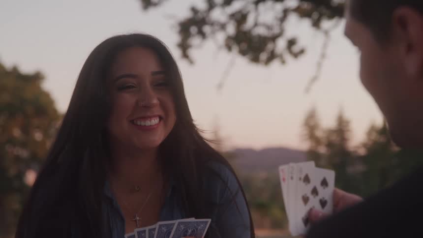 Close up of a young man and woman playing card games outdoors at sunset