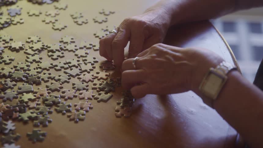 Womans hands wearing a silver ring on her middle finger of one hand and a silver ring on the other hand she is also wearing a silver watch and is putting puzzle pieces together