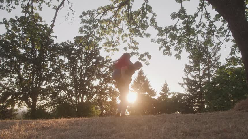 Man carries a woman on his back in a field at sunset
