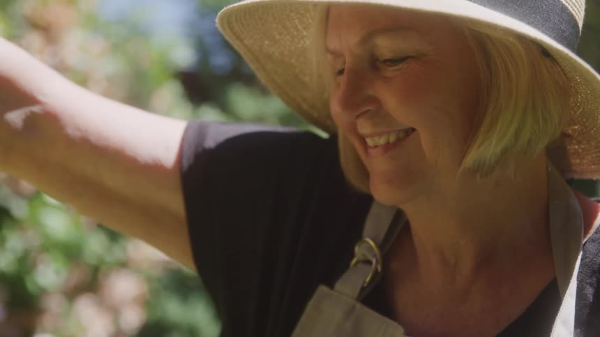 Older blonde woman smiles while working in the garden on a sunny summer day