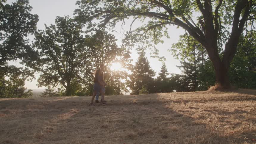 Couple walking across a meadow as the sun filters through the trees in the distance