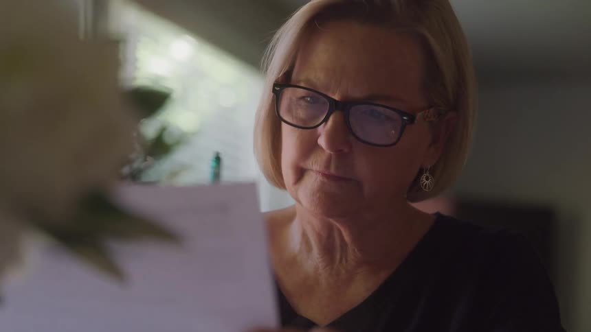 Woman with glasses holds a green pen while carefully analyzing a paper