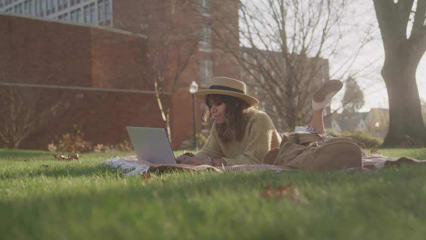 Woman lying on grass working on laptop in a park