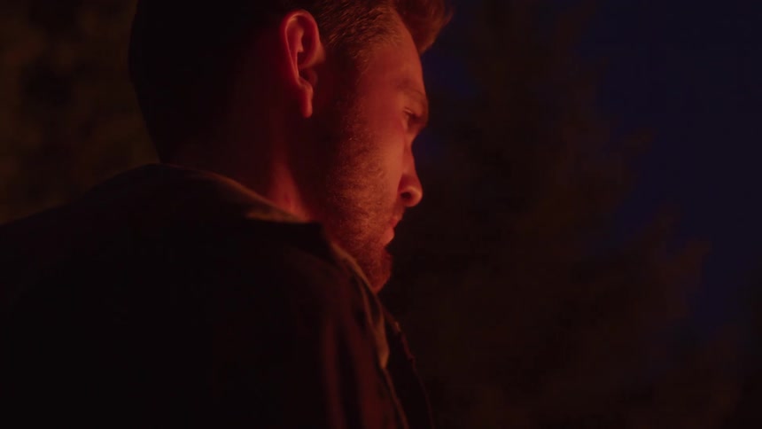 A man gazes ahead his face lit by warm glow against the dark night sky