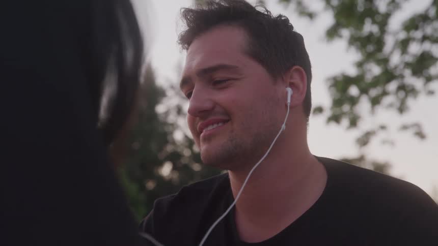 A man wearing a black shirt listen to music sharing earbuds with a woman with her back to the camera