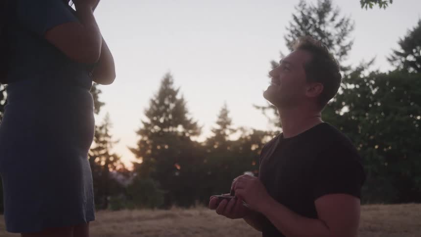 Man kneeling holds a ring box in a marriage proposal outdoors
