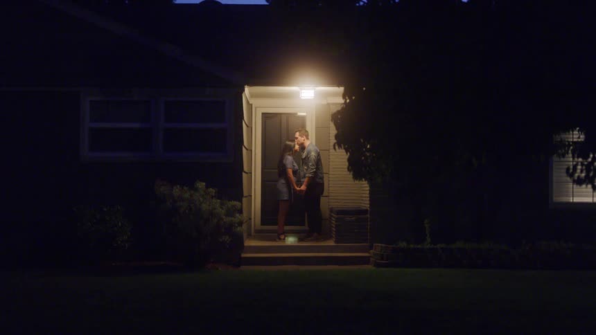 Young teenage couple standing on a porch holding hands boy and girl are chatting and boy kisses the girls forehead it is evening and they seem to be saying good night after a date