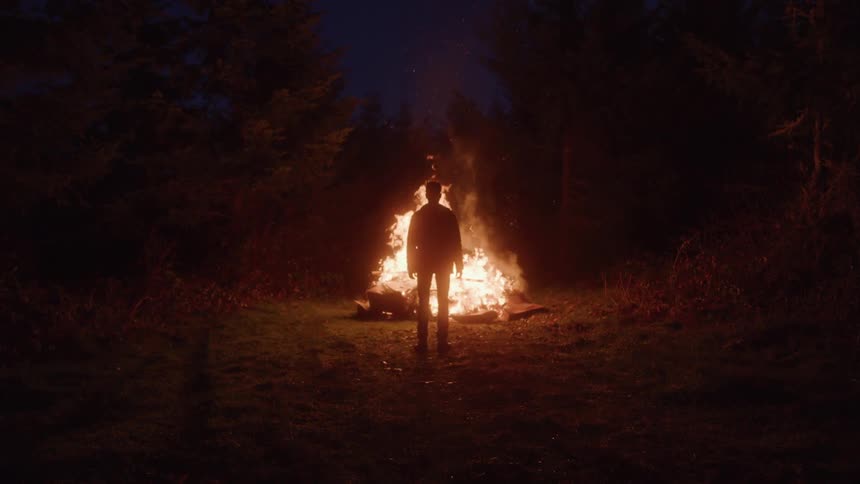 Silhouette of man facing a large bonfire at night