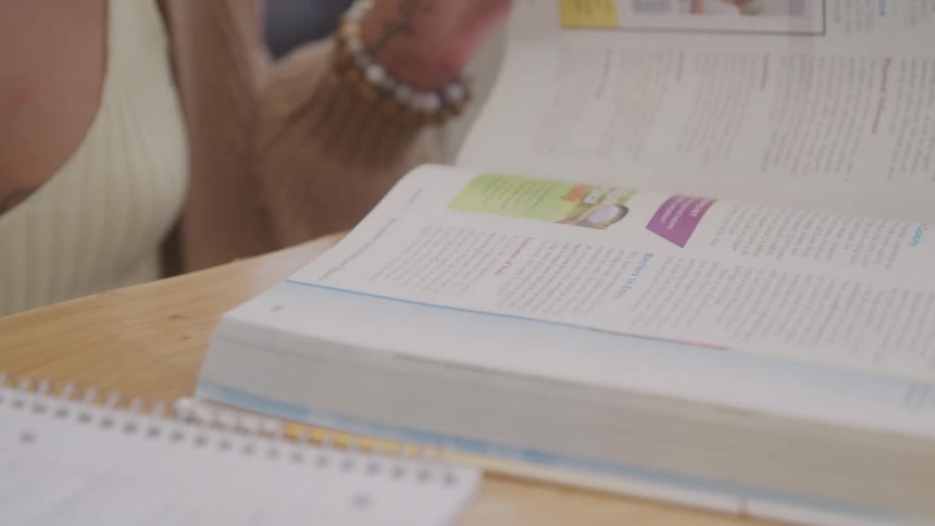 Woman sitting at a table flips through a textbook