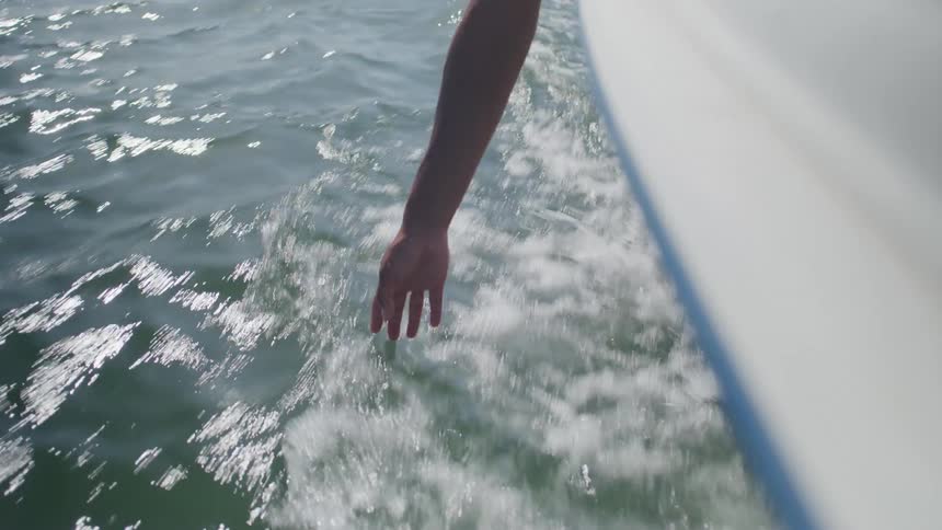 Hand touches the water beside a moving boat