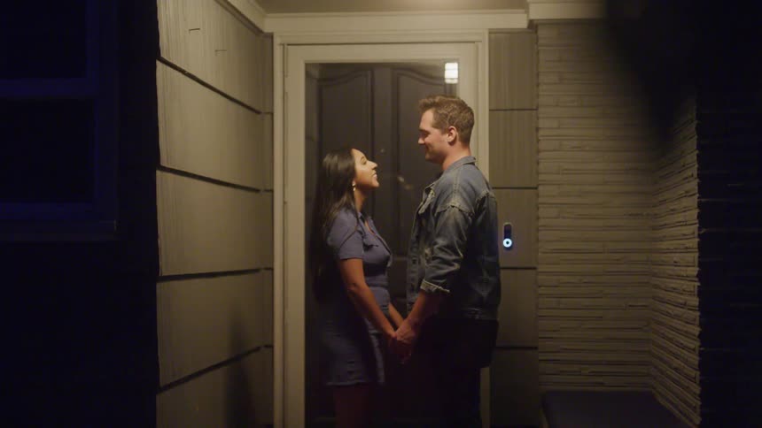 A couple holds hands and leans in for a kiss on a quiet front porch at night