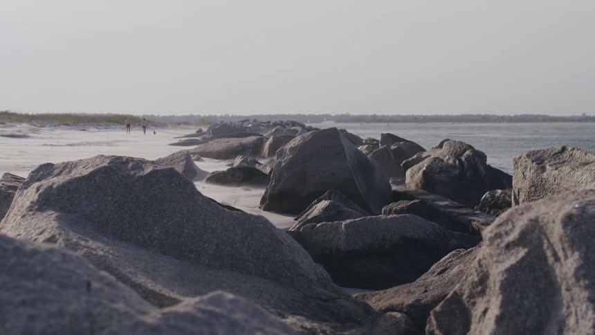 Large rocks line a quiet coastal shore under soft daylight