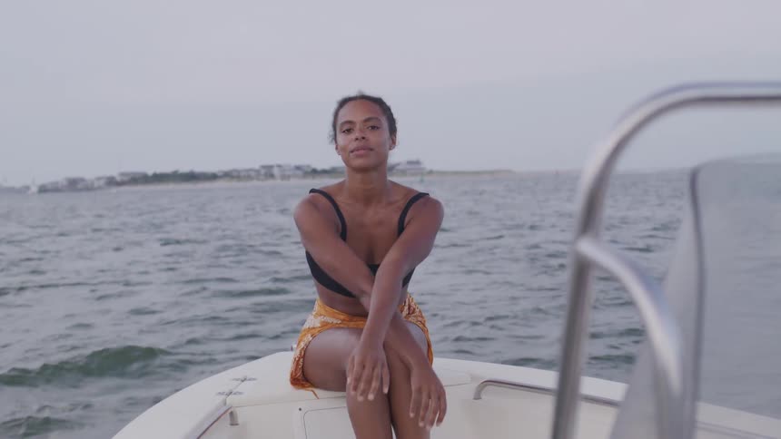 Woman sitting at the bow of a boat crosses her arms and legs in front of the sea