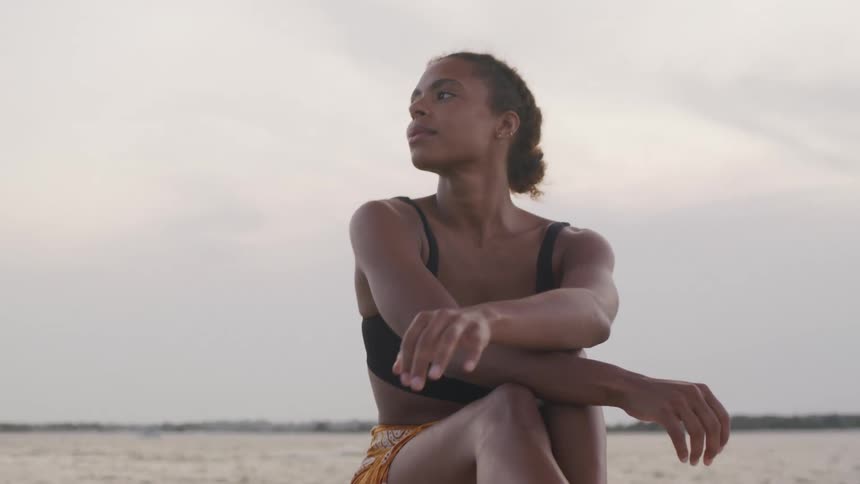 A young woman sits on a boat in the ocean enjoying the atmosphere as the wind blows her clothes at midday