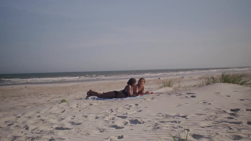 Two friends lay together on a sandy beach and chat