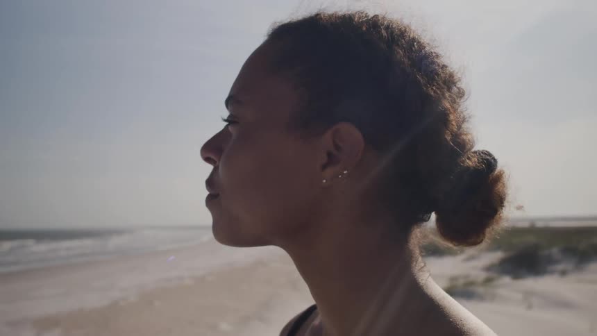 A woman gazes thoughtfully toward the ocean on a sunny beach