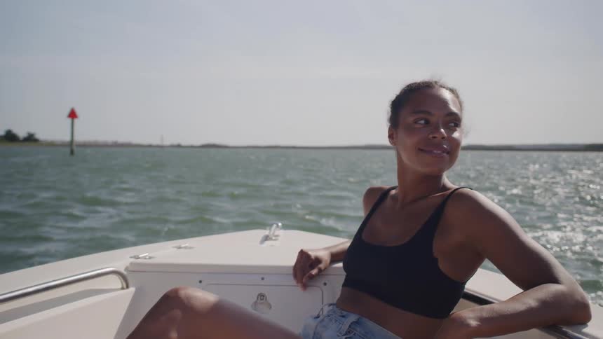 A woman relaxes at the bow of a boat under bright midday sun with rippling water behind her