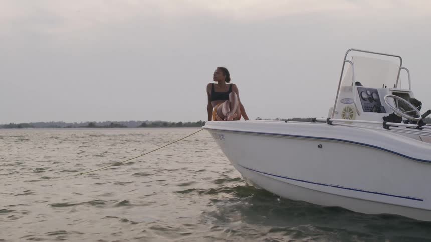 Woman sitting at the bow of a boat gazes at the horizon at dusk