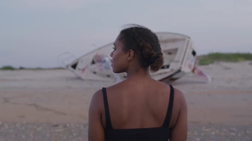 A woman on a beach with a capsized boat