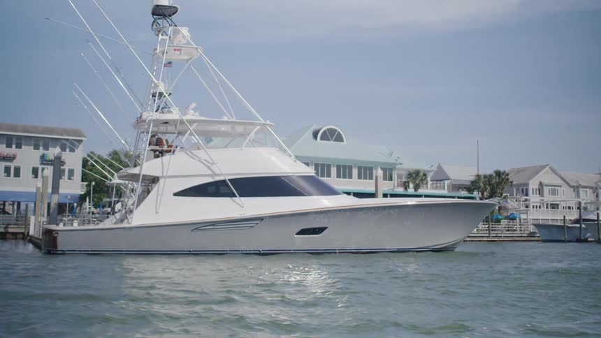 A yacht is docked near a marina with waterfront buildings in the background