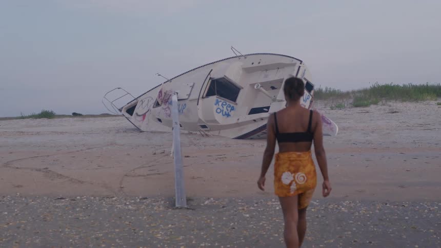 A woman walks towards a capsized boat