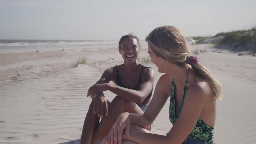 Two women smiling while sitting on the beach sand
