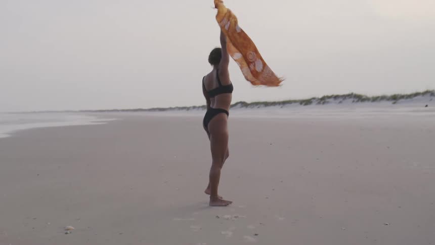 A woman walks confidently and happily along an empty beach at dusk