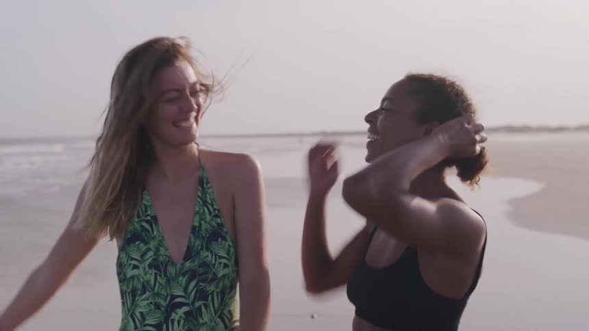 Two young women are laughing while walking on the beach