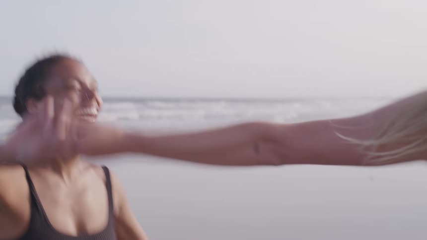 Two girls walking along the beach one is a black female with french braided hair and the other is white and blond with straight hair they are laughing and holding hands as they walk the white girl spins the black girl as if they are doing a dance move