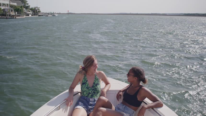 Two women relax smiling on the bow of a moving boat
