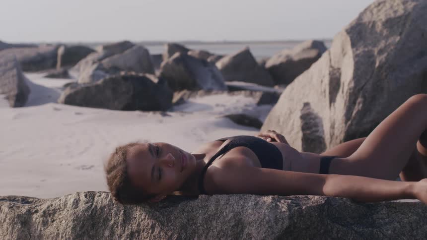 A woman lays on the rocks near the water