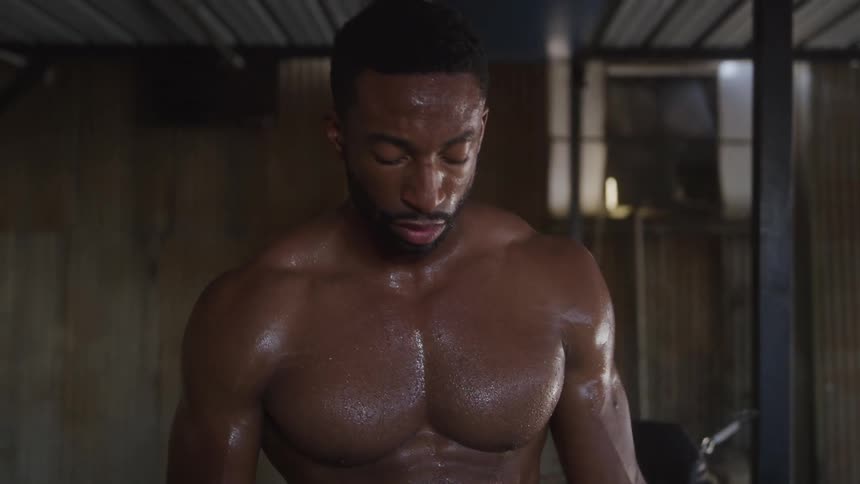 Muscular bare chested man stands sweating in a wood paneled room